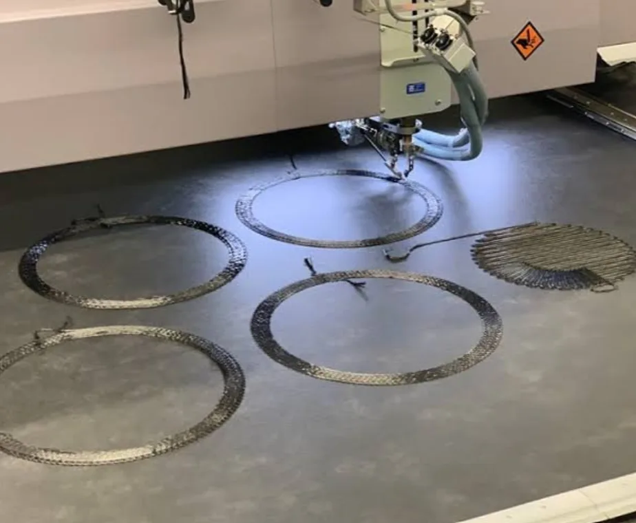 A tailored fiber placement head stitching large circular carbon fiber ring preforms laid out across a machine bed.